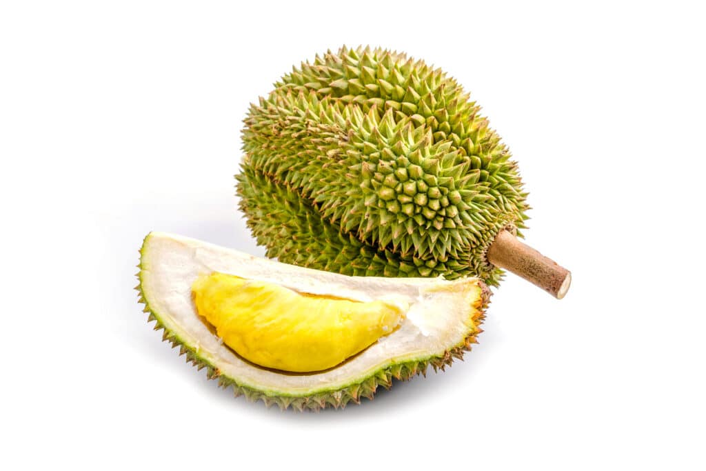 Greenish oval shaped durian fruit with a quarter slice next to it showing the inside of the fruit.