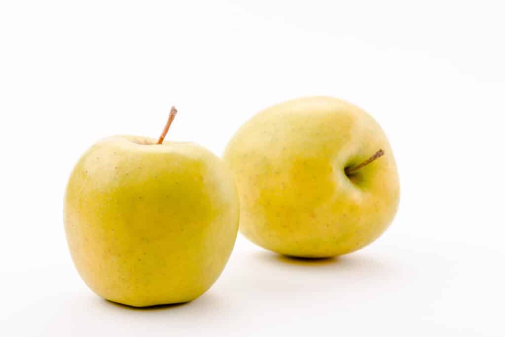 Two gold colored apples on a white surface.