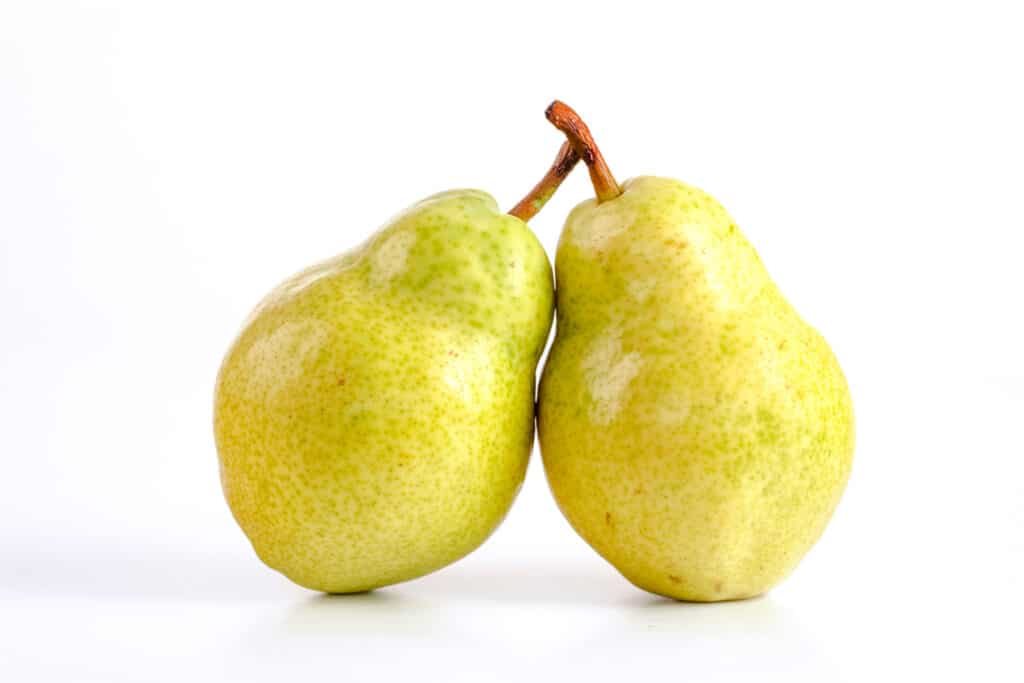Two yellow-green pears leaning against each other on a white surface.
