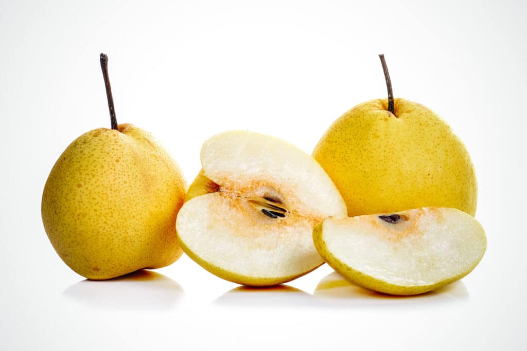 Three Asian pears with one cut open showing its seeds.