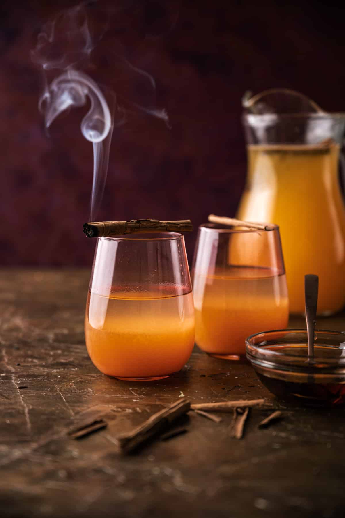 Two cups and a pitcher of pumpkin lemonade with smoking cinnamon sticks.