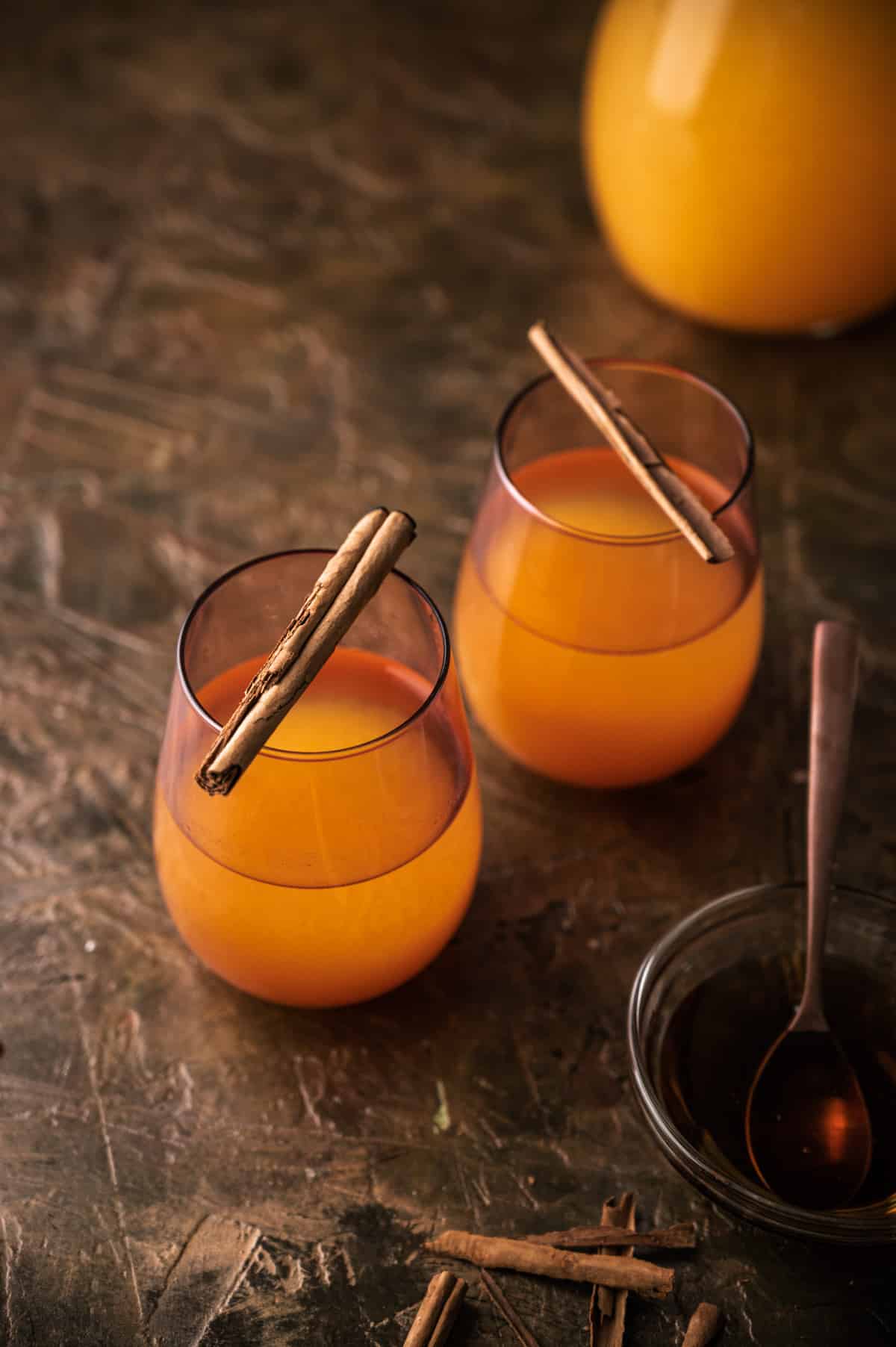 Two cups of pumpkin lemonade with cinnamon sticks across the lip of the glass. 