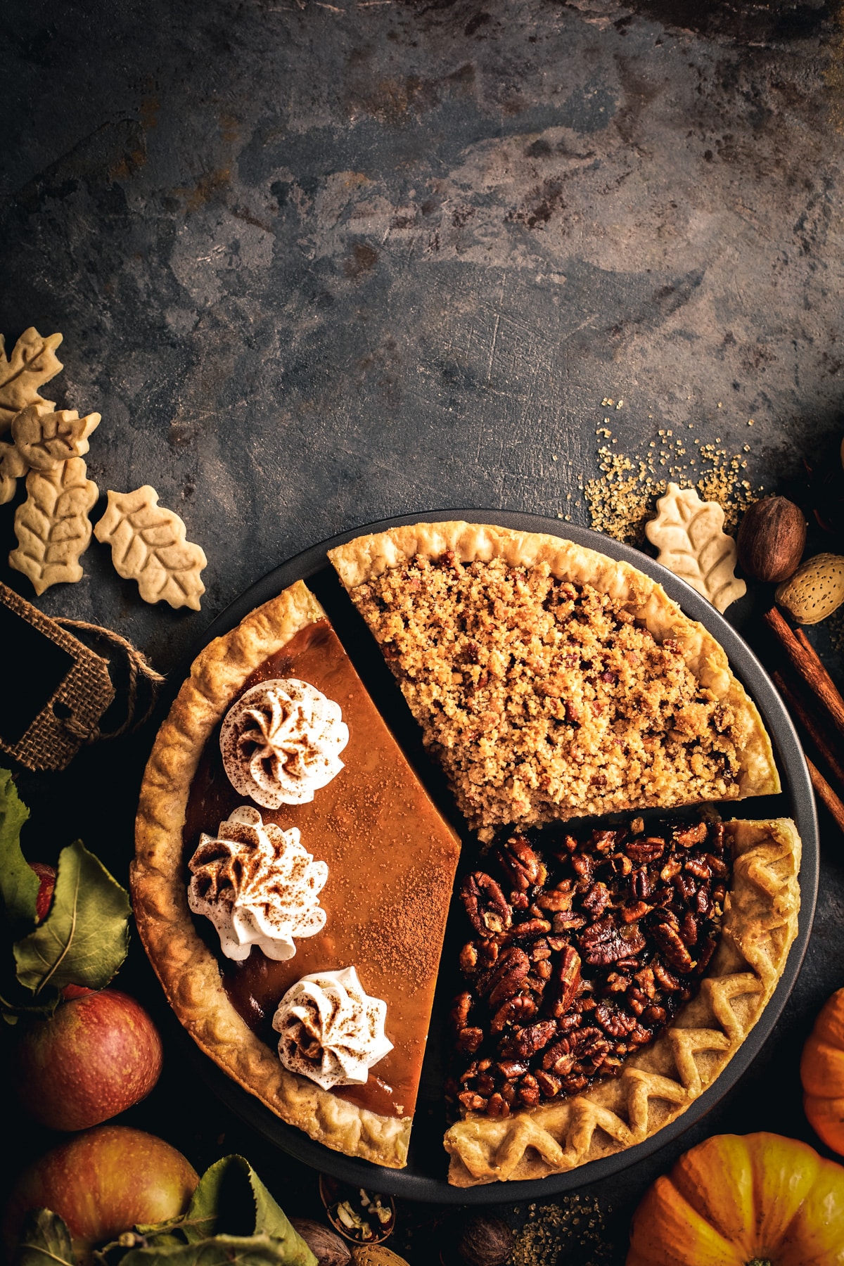 One third of three different pies put together in a pie pan with fresh fall produce around. 