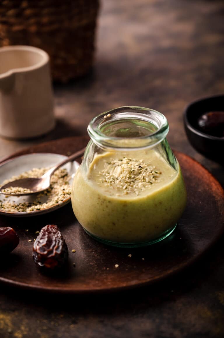 Avocado smoothie in a glass cup with a spoon in front of it with hemp seeds on it.