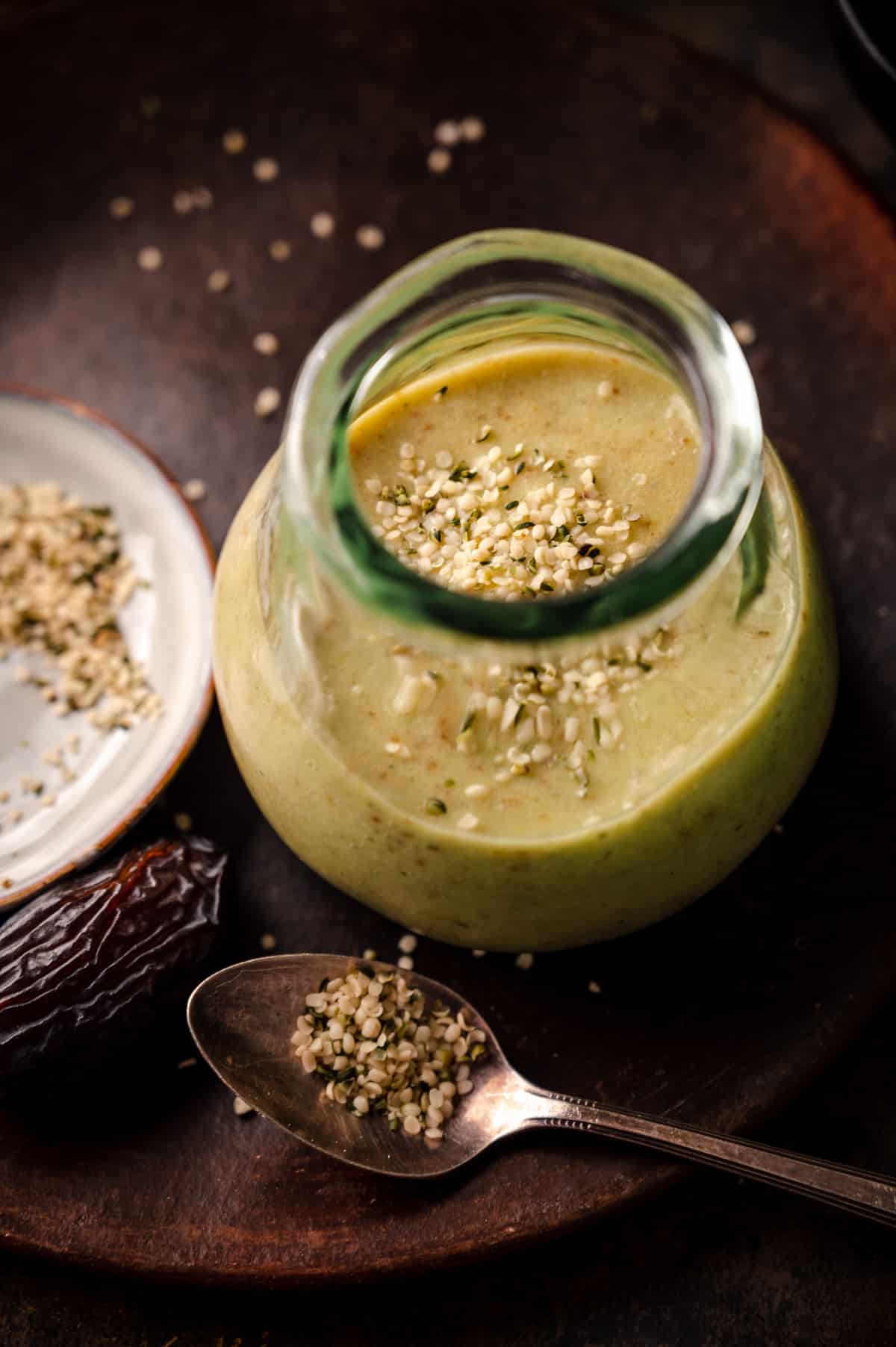 Fresh avocado smoothie in a clear glass cup on a plate with hemp seeds sprinkled on top.
