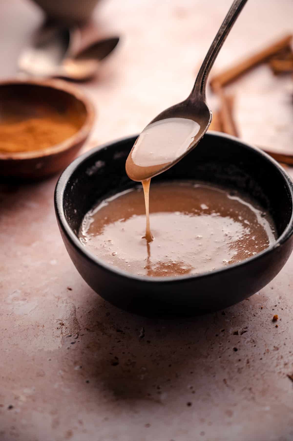 Bowl of cinnamon glaze with a spoon drizzling it into the bowl.