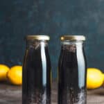 Two glass bottles of charcoal lemon chia drink with lemons behind it.