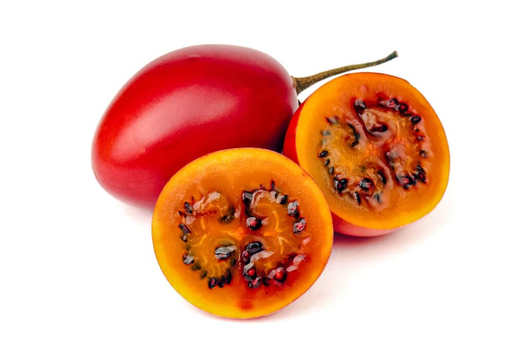 Red to orange tamarillo fruit showing its orange flesh and black seeds.