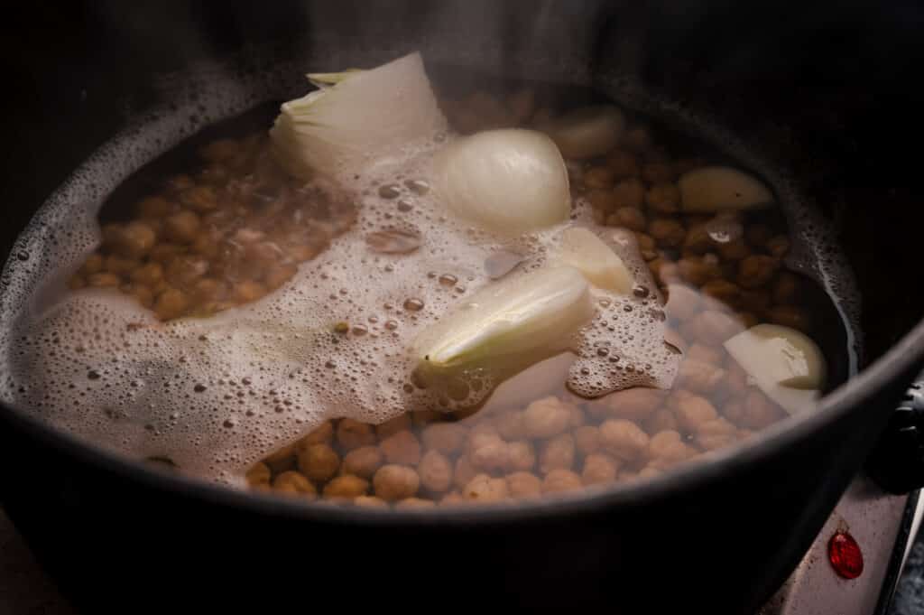 Garbanzo beans boiling in water with aromatics.