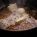 Garbanzo beans boiling in water with aromatics.