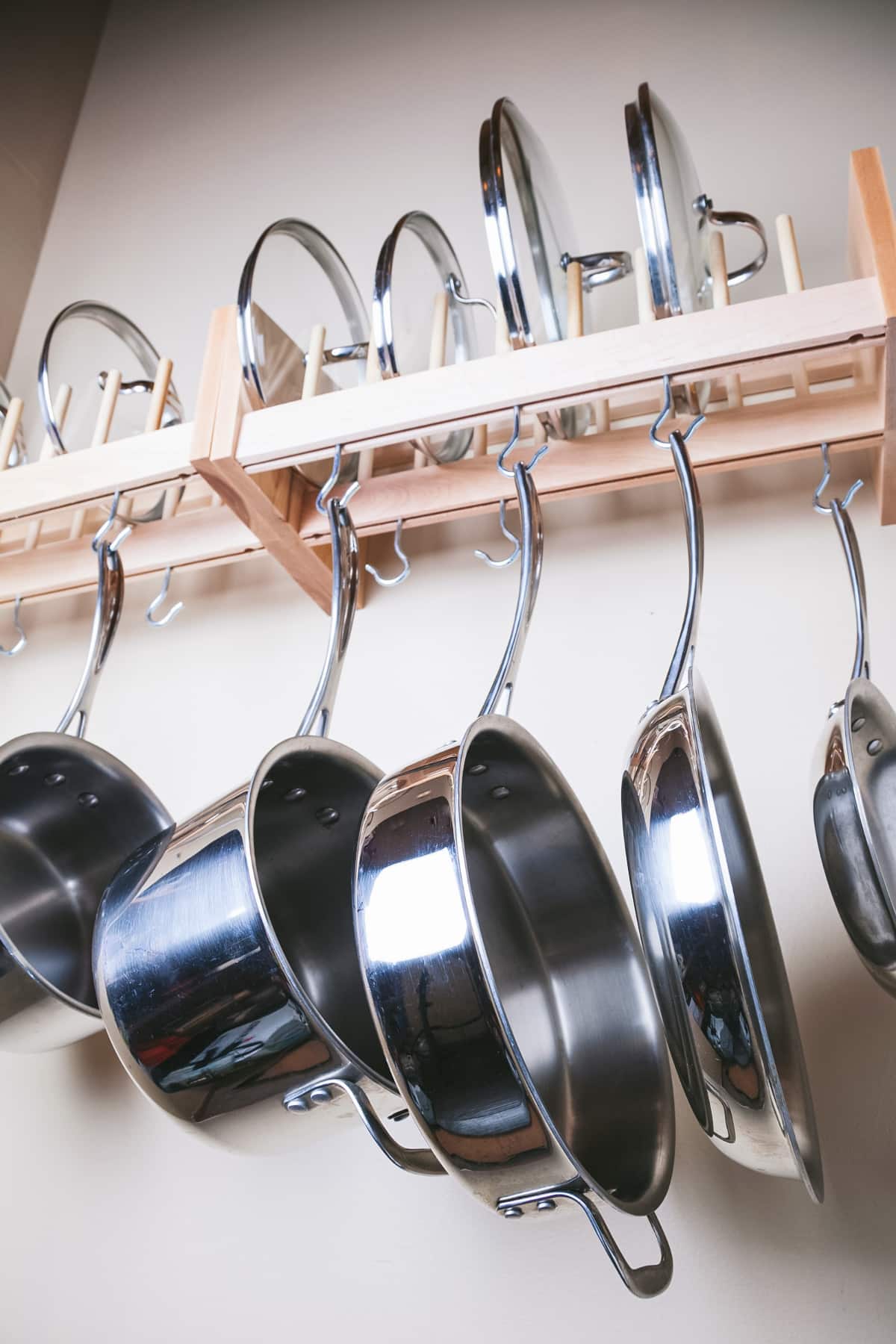 Stainless steel pots and pans hanging from a wooden shelf.