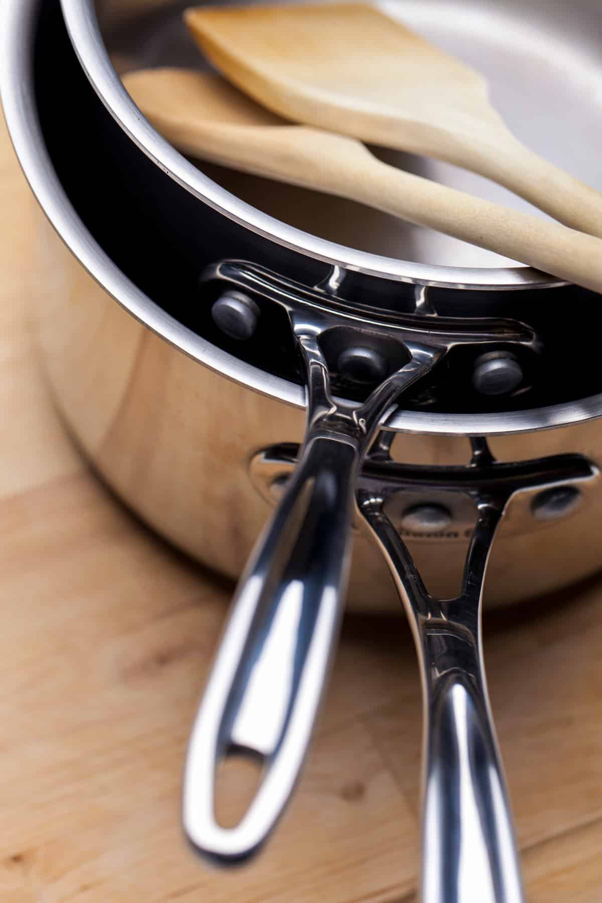 Two stainless steel saucepans stacked with two wooden spoons.