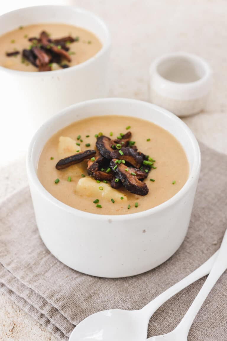 Two small bowls of creamy soup with vegan bacon on top.