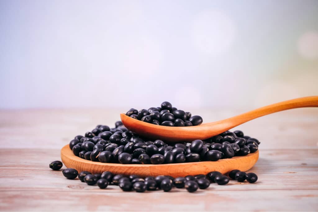 Wooden plate over flowing with black beans with a wooden spoon on top overflowing with black beans.