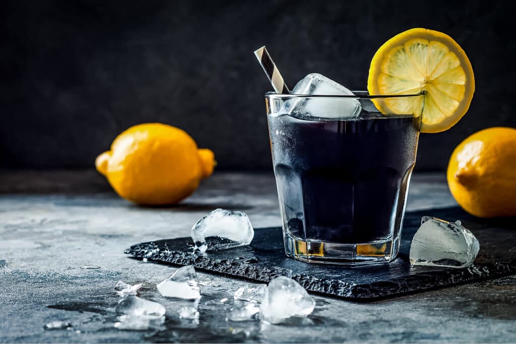 Black lemonade in a clear glass cup with fresh lemon slice on the rim.