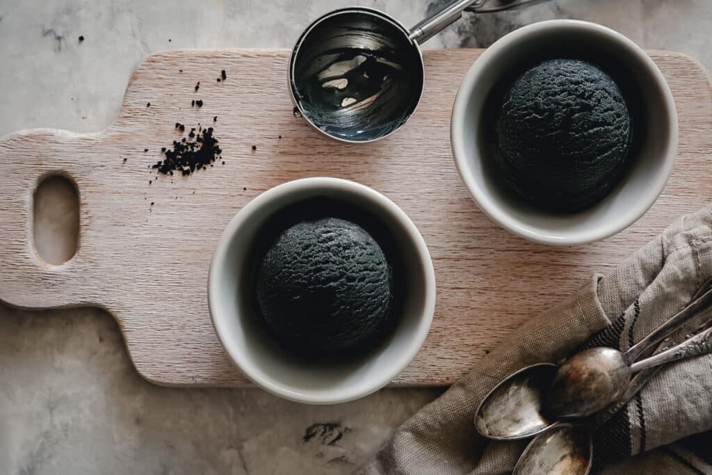 Black charcoal vegan ice cream in white bowls on a wooden serving board.