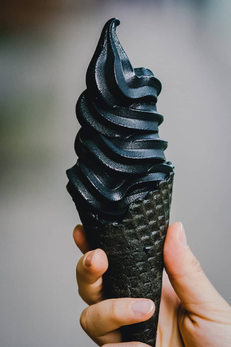 Person holding deep black soft serve ice cream in a black waffle cone.