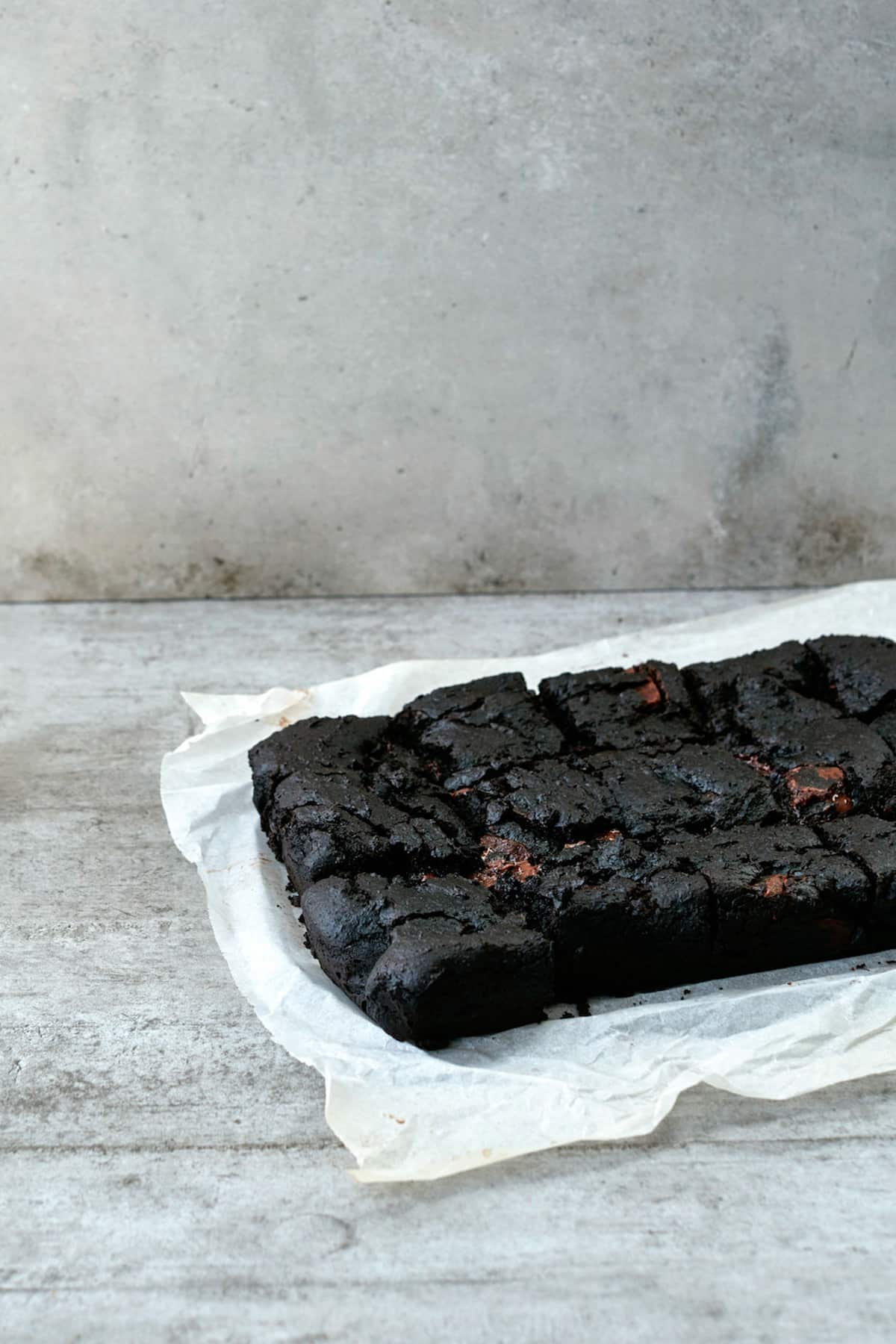 Black brownies on on a piece of parchement paper.