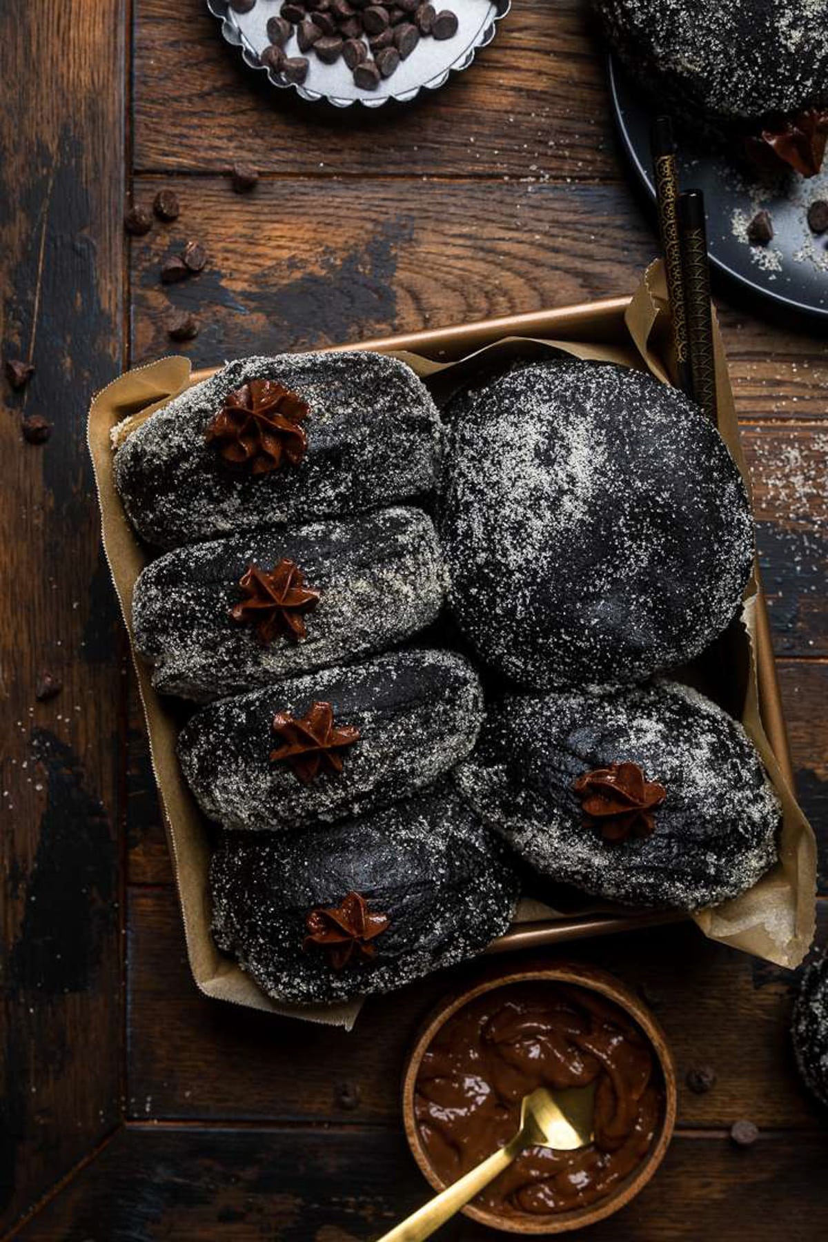Black chocolate stuffed donuts in a baking pan lined with brown parchment paper.