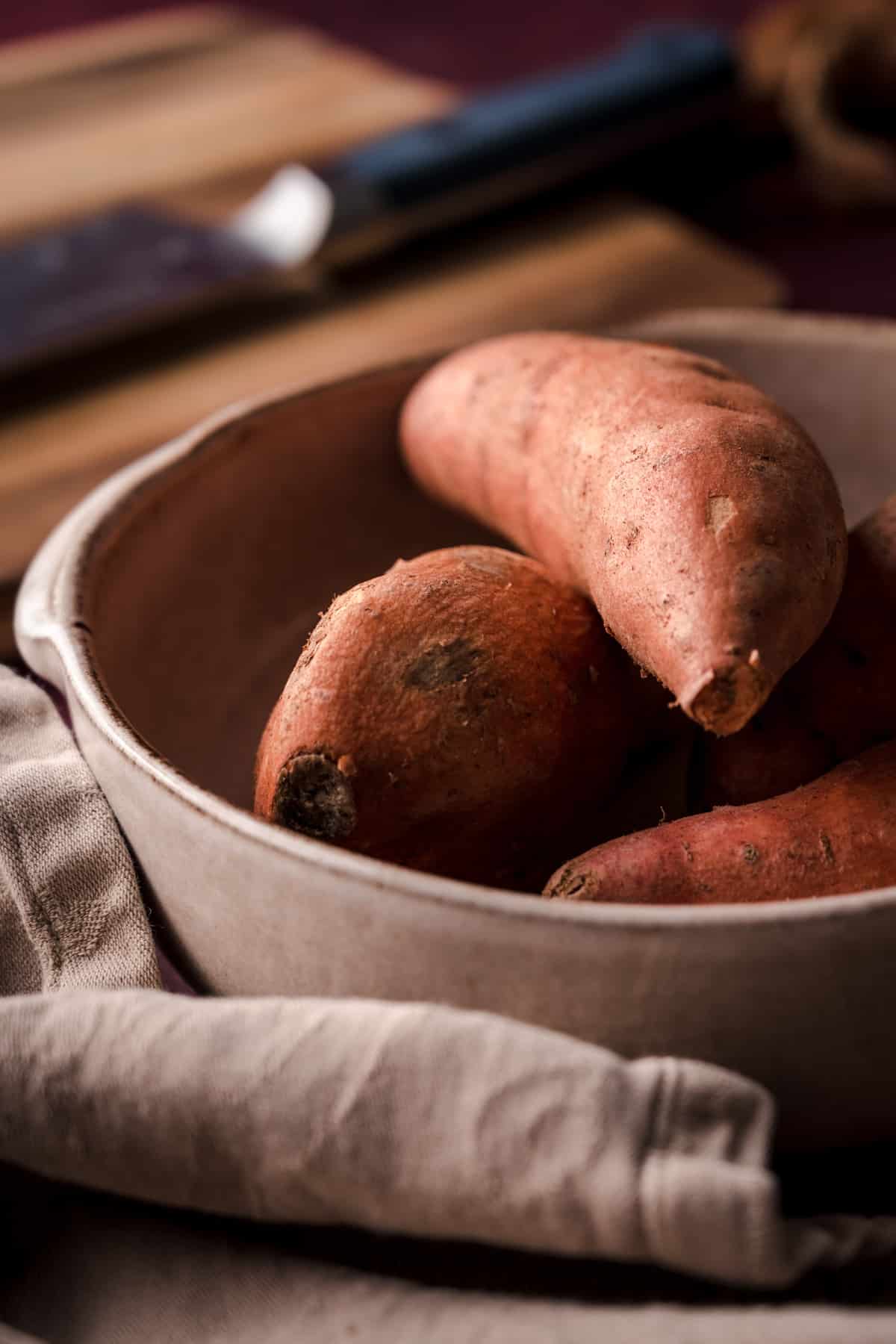 Ceramic bowl with several sweet potatoes in it.