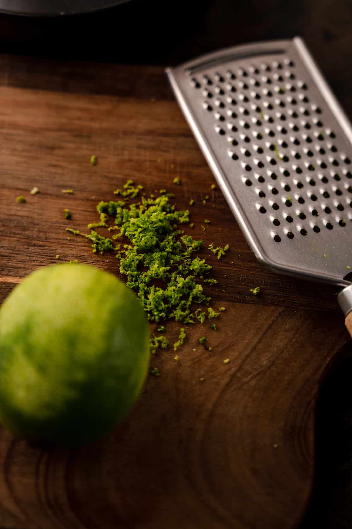 Fresh lime zest on a wooden cutting board with a citrus microplane on top.
