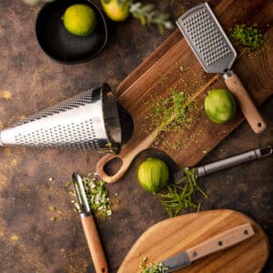 Wooden cuttings boards with five different zesting tools, limes and their zest scattered about.