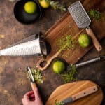 Wooden cutting boards and citrus zesters with a woman's hand picking up a veggie peeler.