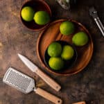 Wooden tray full of limes with different zesters and a circular box grater.