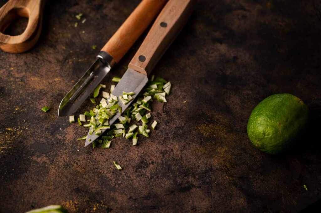 Wooden vegetable peeler and a paring knife with a lime next to them.