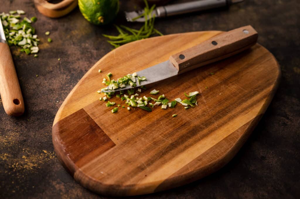 Paring knife with wooden handle finely chopping up lime skin to make zest.