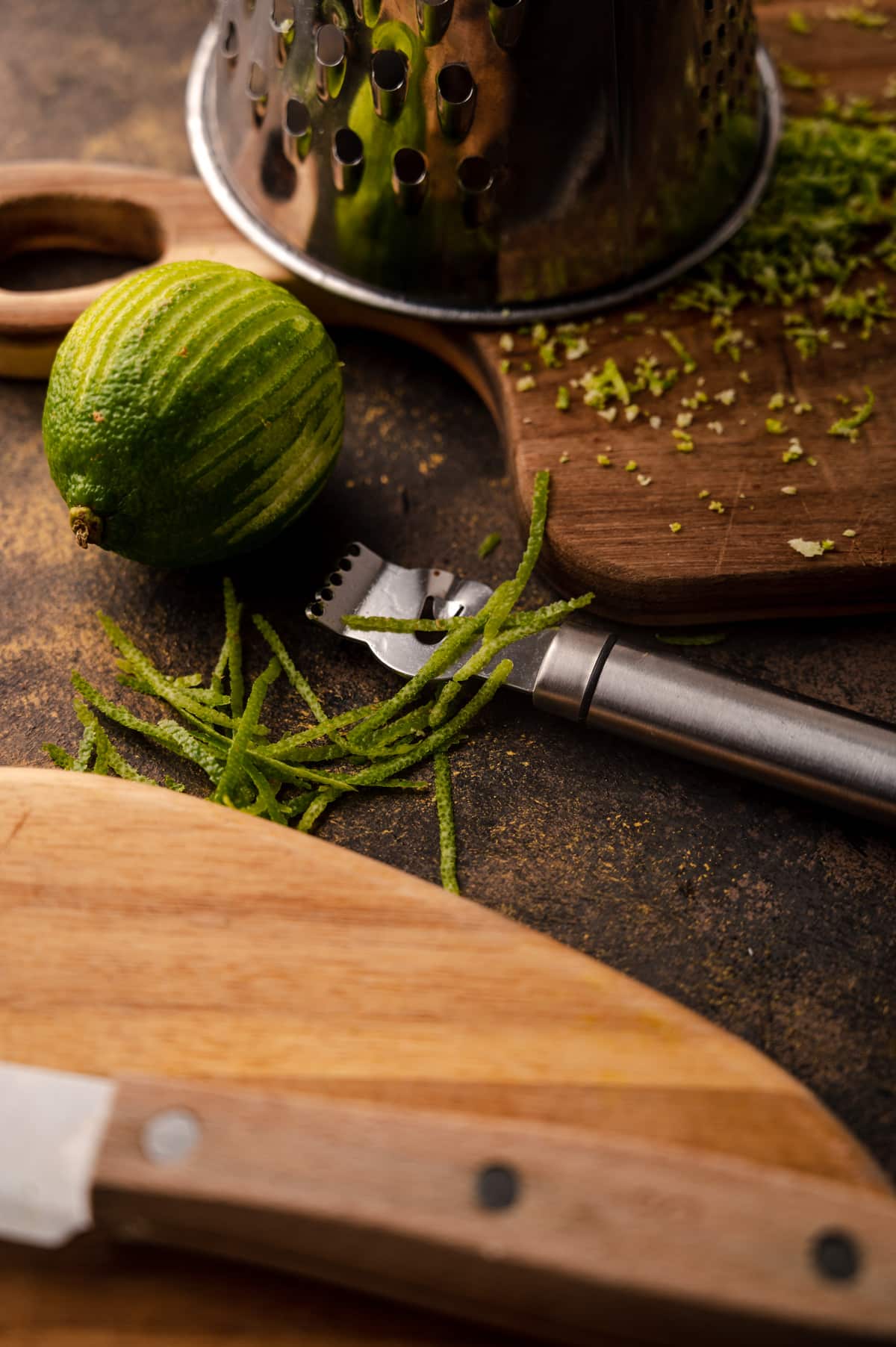 A whole lime next to a ribbon zester and wooden cutting boards.