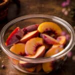 Frozen yellow peaches in a round glass freezer safe container.