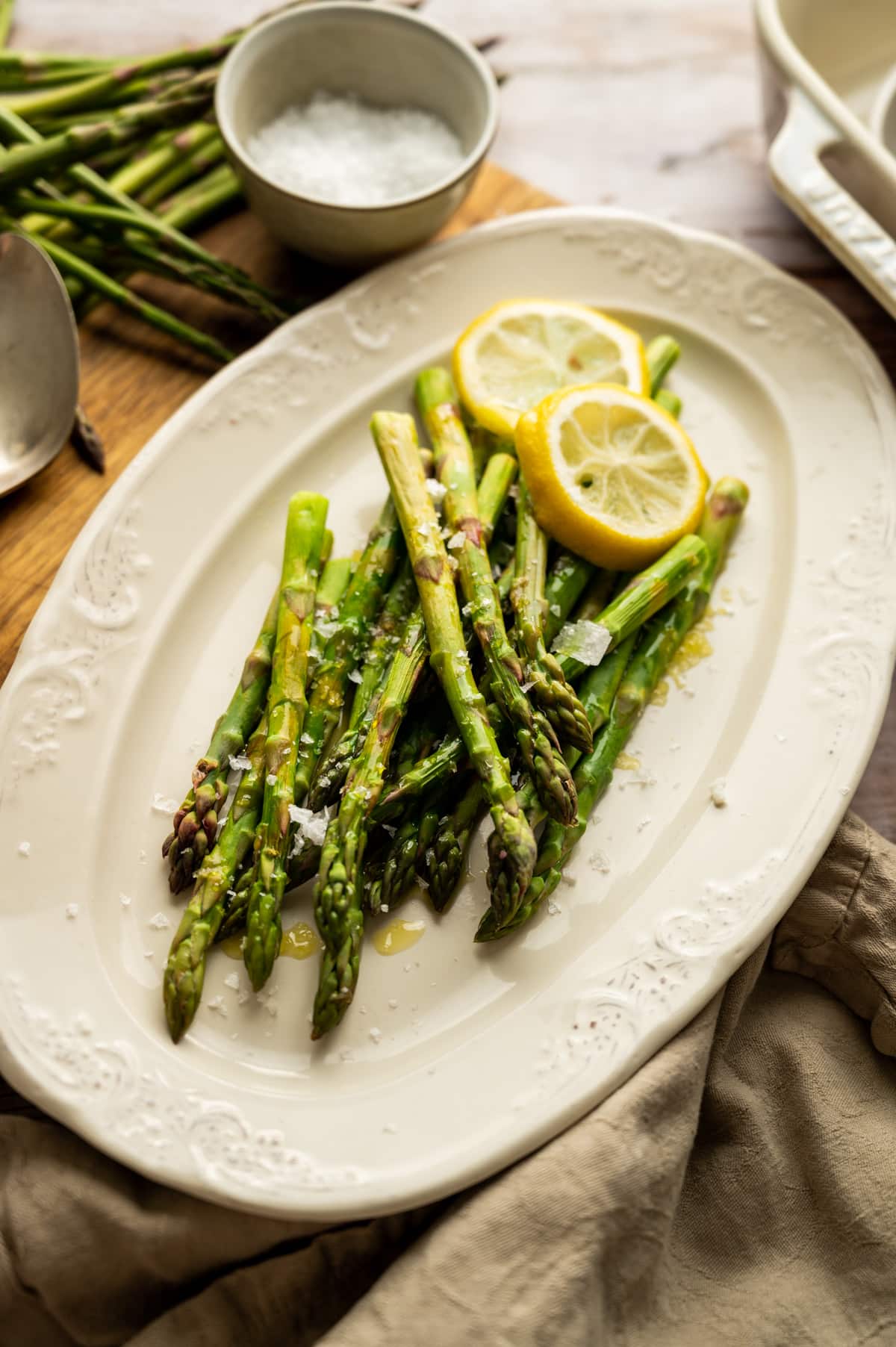 Freshly microwaved asparagus with two lemon slices on top and a tan cloth napkin to the side.
