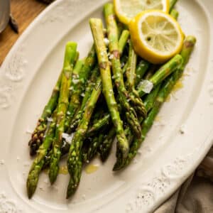 Large cream plate with cooked asparagus and lemon slices.
