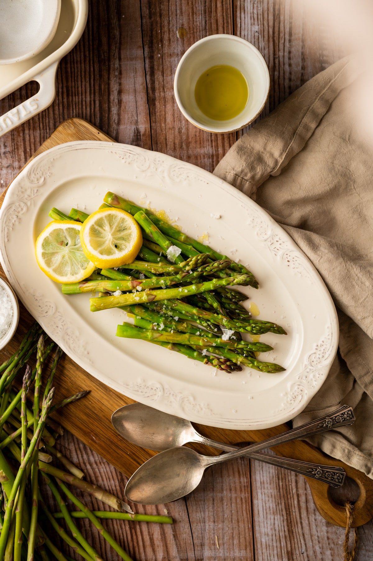Cream colored plate with cooked asparagus on top and fresh asparagus to the side.