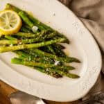 Close up of oval plate piled with asparagus and cloth napkin to the side.