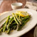 Angled close up view of green asparagus on an oval plate with lemon slices.