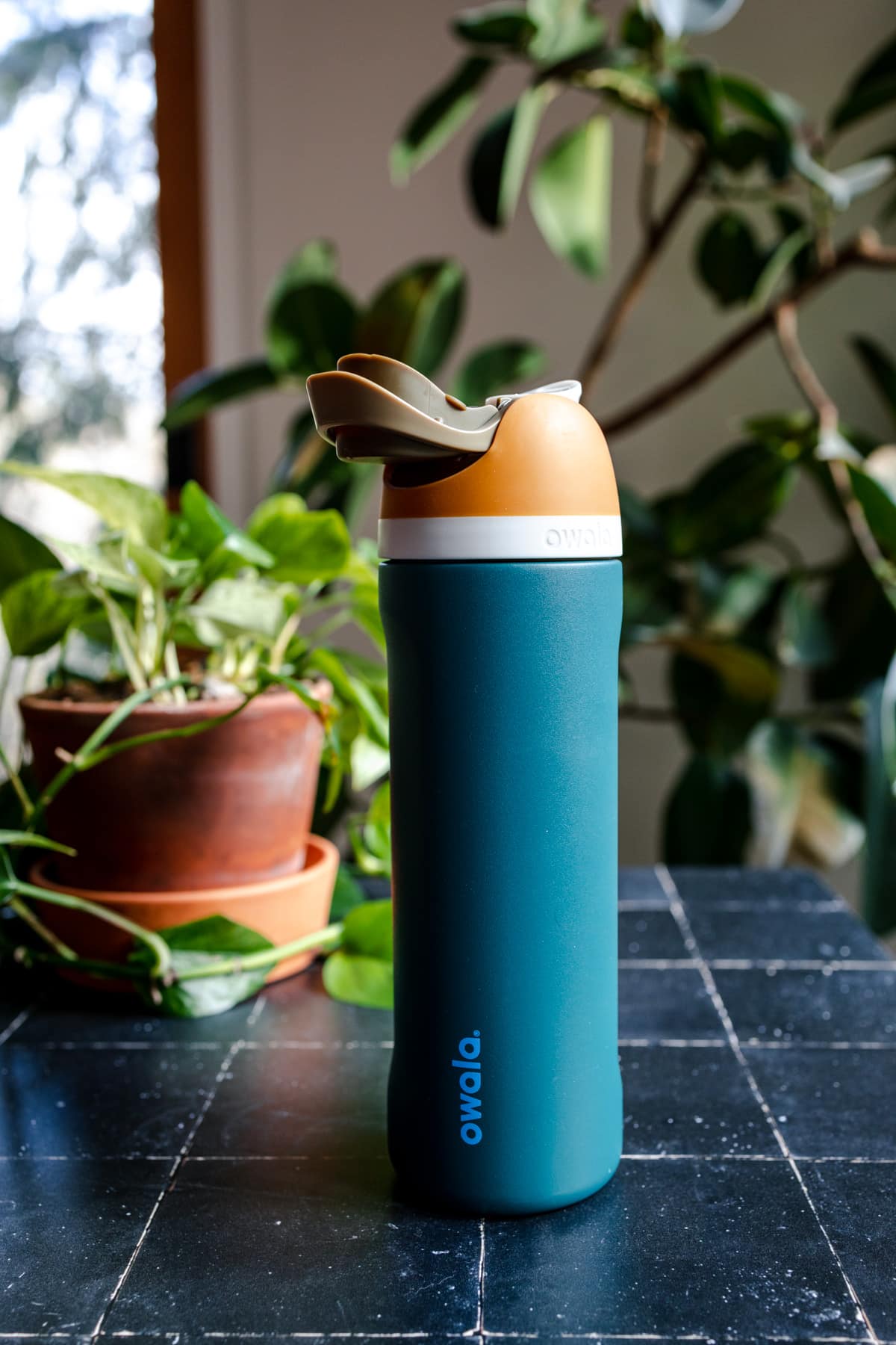 Teal Owala waterbottle that is opened sitting on a black tile surface.