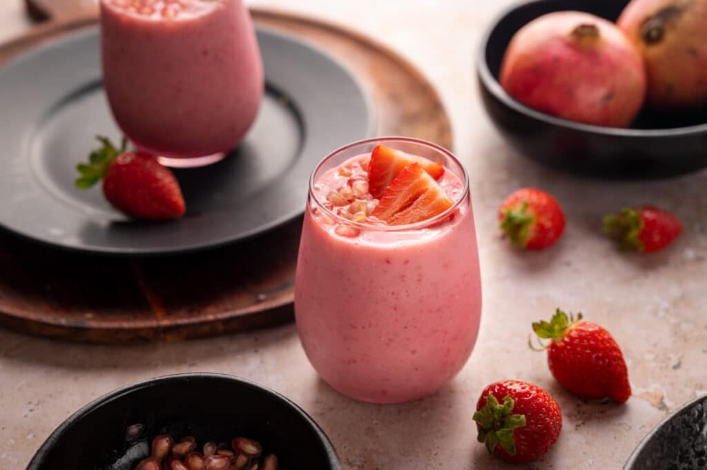 Light pink glass full of pomegranate smoothie topped with arils and strawberries.