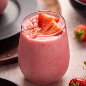Pink glass filled with pomegranate smoothie topped with sliced strawberries and pomegranate arils.