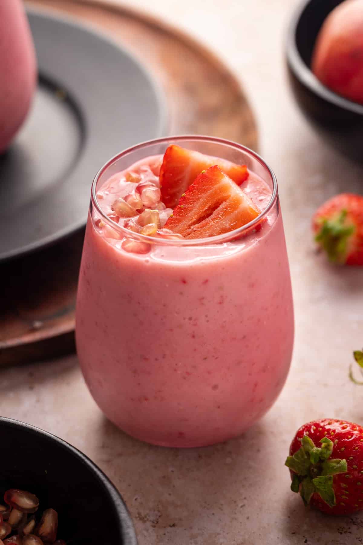 Pink glass filled with pomegranate smoothie topped with sliced strawberries and pomegranate arils.