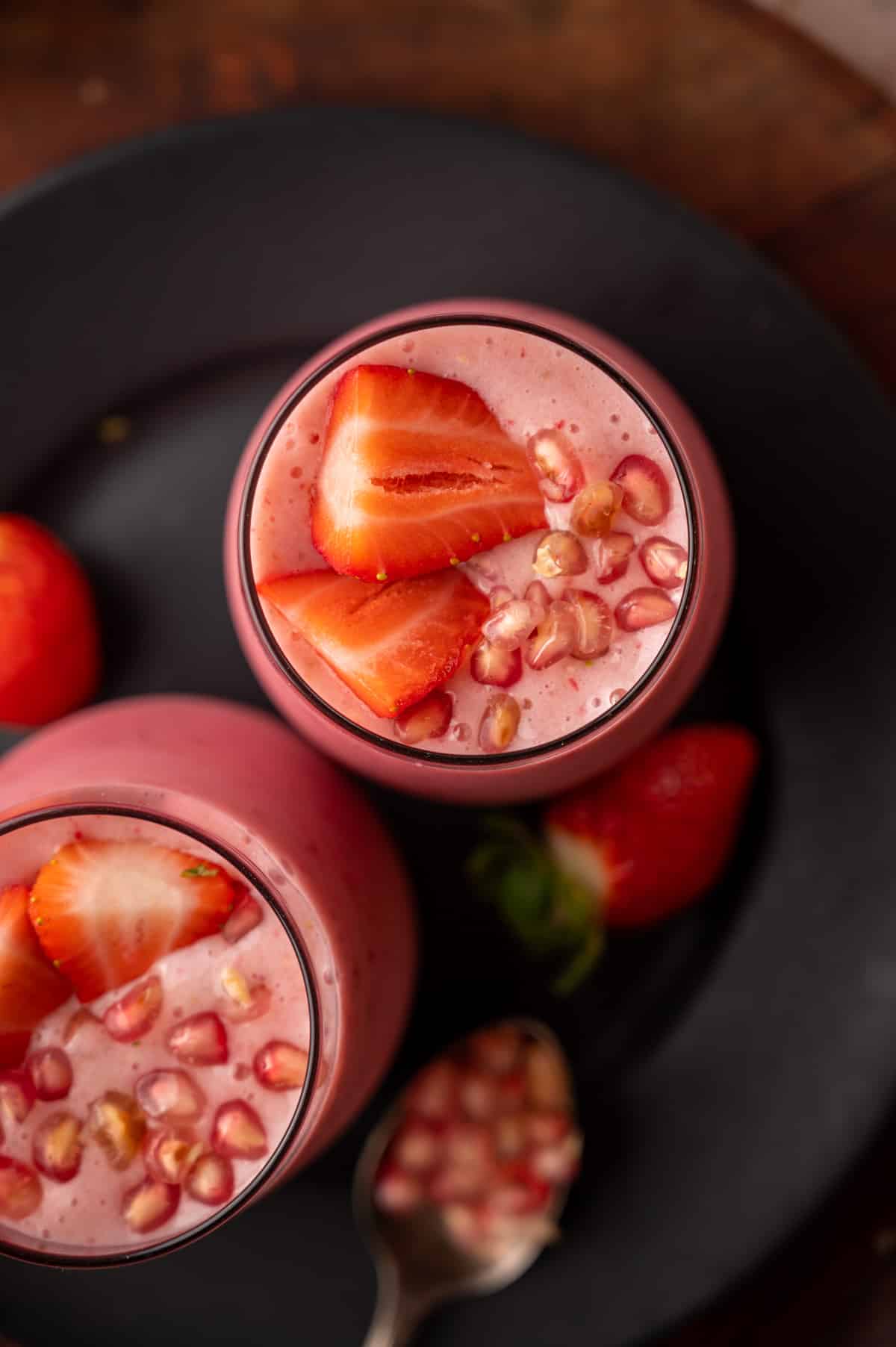 Close up of pomegranate smoothie with arils nad strawberry slices.