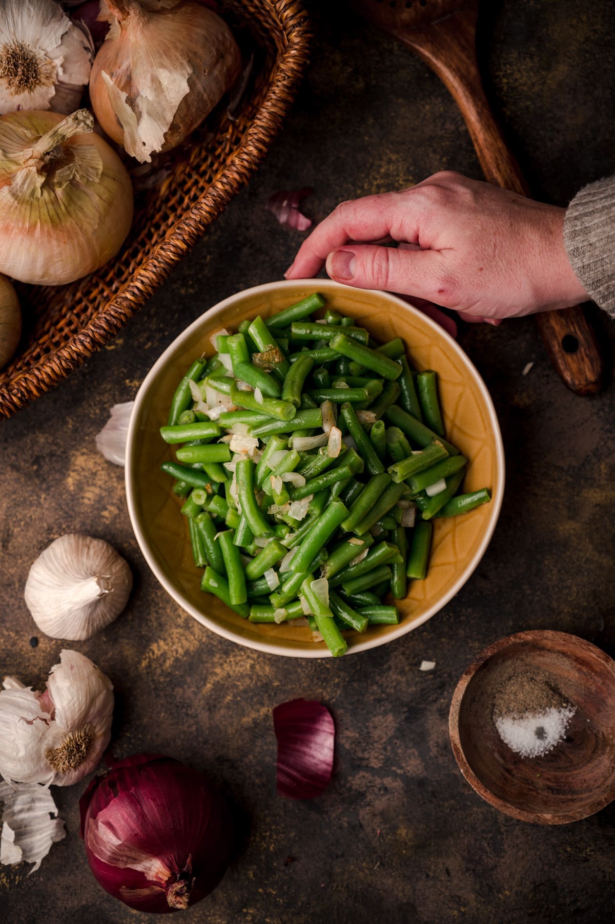 Woman reaching for a golden yellow bowl of cooked canned green beans.