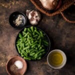 Bowl of canned green beans with ingredients in small bowls surrounding it.
