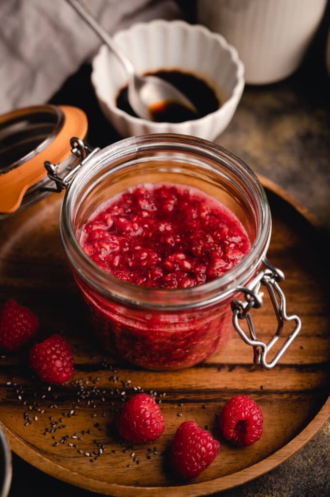 Glass jar full of raspberry chia jam on a wooden plate.