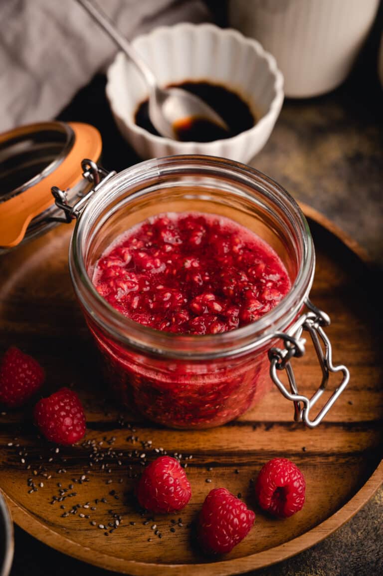 Glass jar full of raspberry chia jam on a wooden plate.