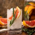 Glass of grapefruit infused water with sliced grapefruit and sprigs of rosemary on the wooden table.