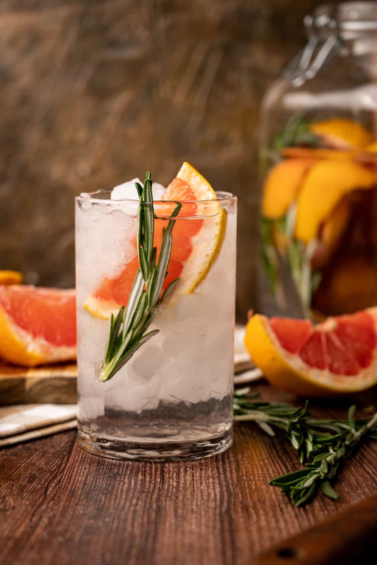 Glass of grapefruit infused water with sliced grapefruit and sprigs of rosemary on the wooden table.