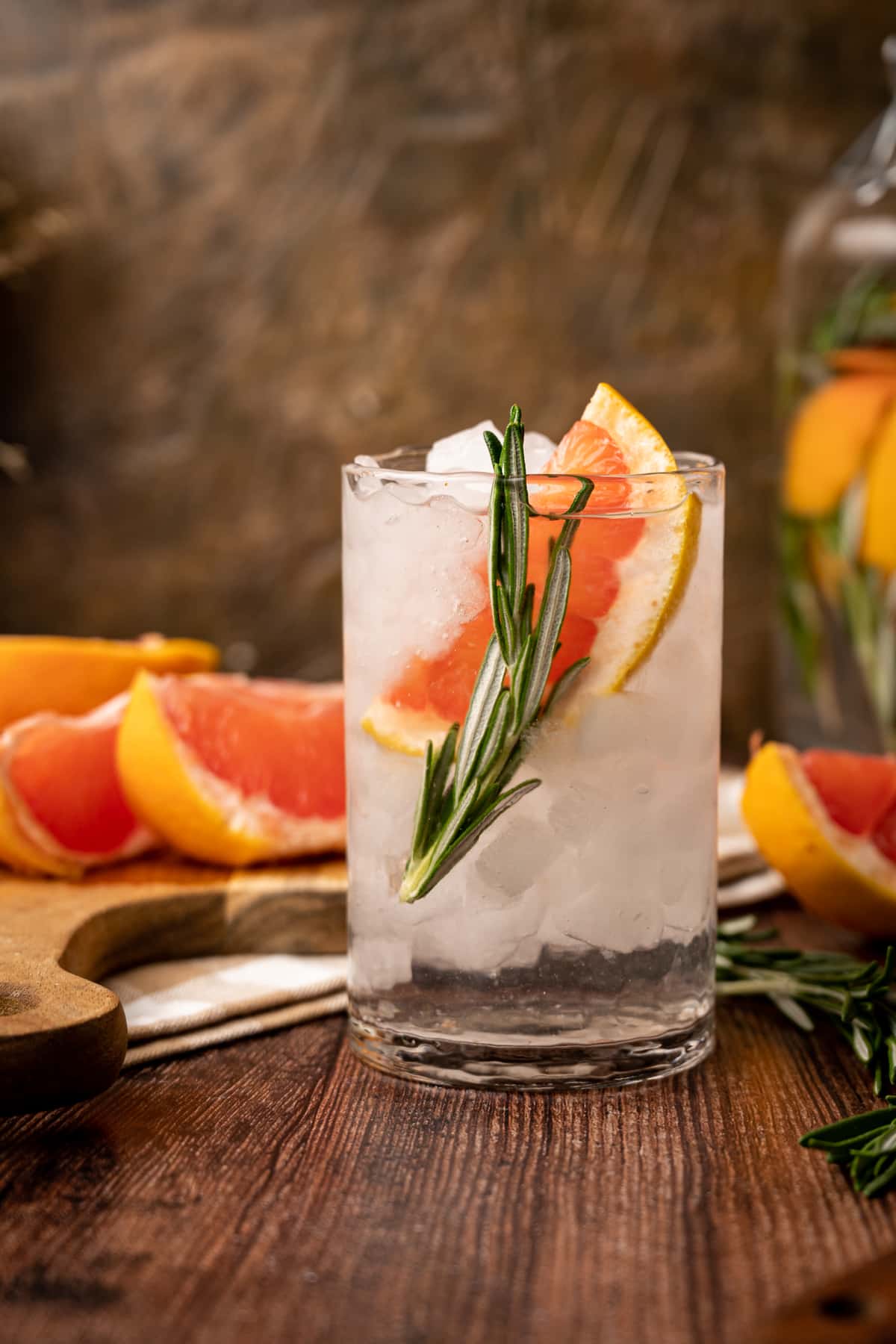 Clear glass cup of infused grapefruit water with a slice of grapefruit and a sprig of rosemary.