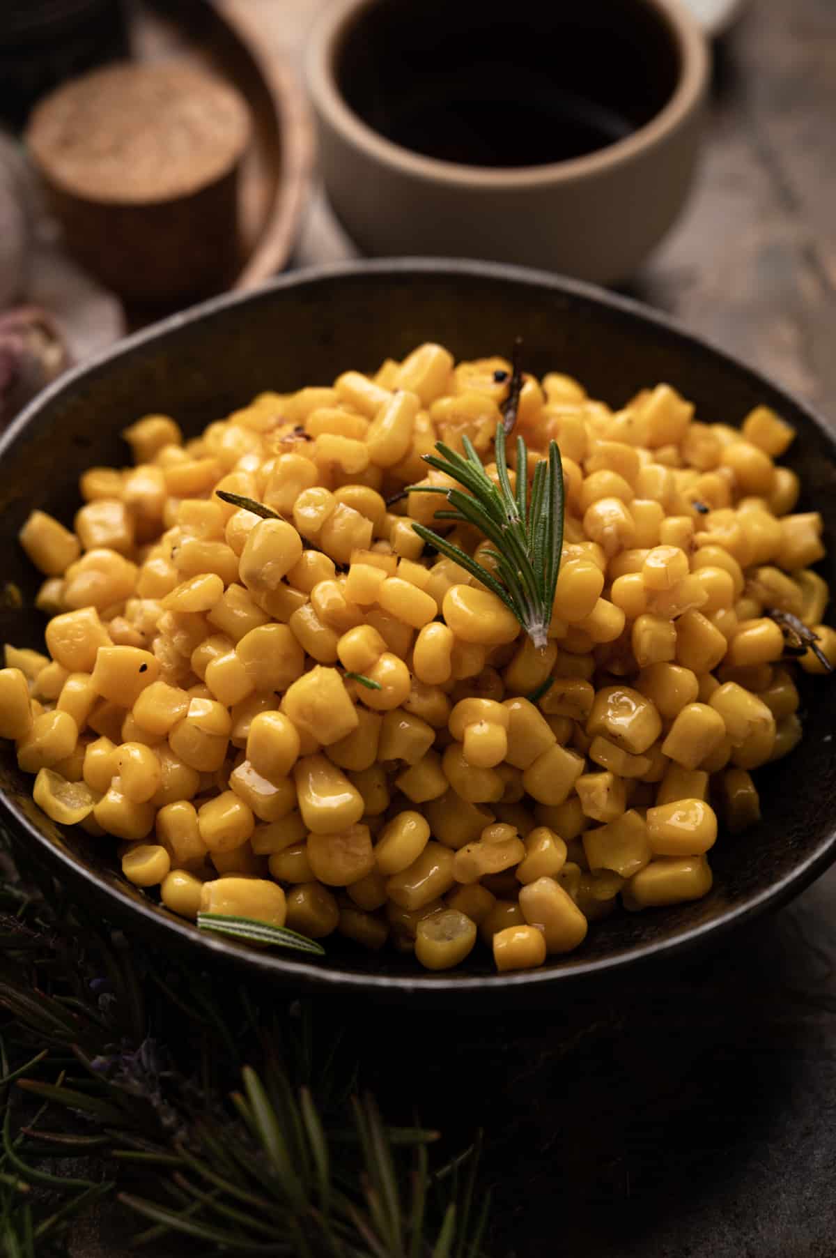 Bowl of cooked canned corn with fresh rosemary on top.